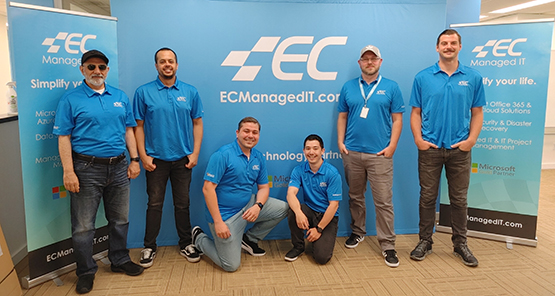 Six men posing in front of a EC Managed IT poster