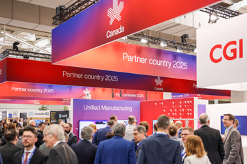 © Deutsche Messe AG. The busy HANNOVER MESSE exhibition hall featuring Canada as the partner country for 2025, with large banners overhead and a crowd of attendees networking and visiting various technology and manufacturing displays.