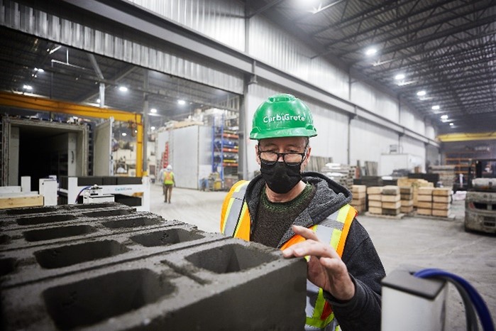 Une personne portant un gilet de sécurité et un casque vert inspecte un bloc de ciment.