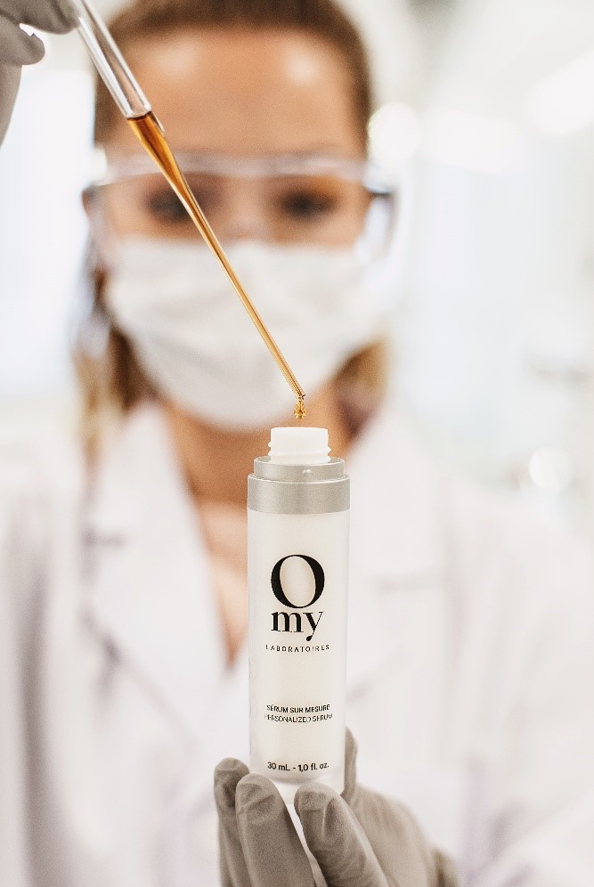 Un employée de laboratoire masquée ajoute des gouttes dans une bouteille d’Omy Laboratoires à l’aide d’une pipette.