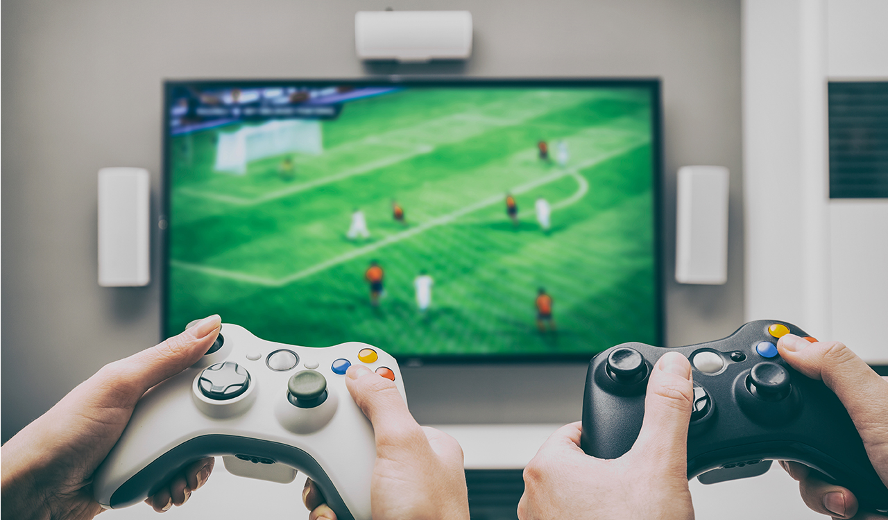 Deux personnes, manettes de jeu en main, jouent à un jeu vidéo de soccer à la télévision