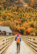 Randonneur franchissant un pont de bois près d'une zone boisée en automne.  